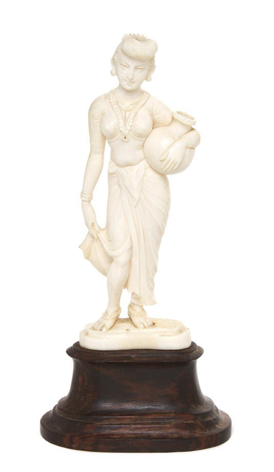 An Indian Ivory Carving of a Lady, Height overall : An Indian Ivory Carving of a Lady, depicted in a standing position holding a bulbous jar, holding up one corner of her sari, raised upon an attached, shaped ivory base, further raised on a shaped hard