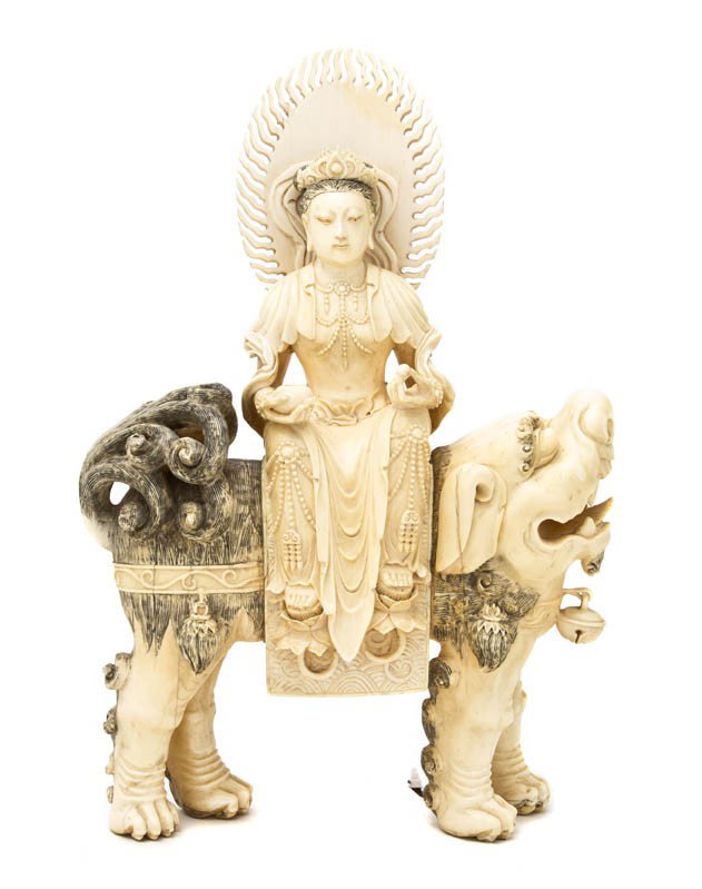 A Carved Ivory Figure of a Deity, Height 11 1/2 in: A Carved Ivory Figure of a Deity, depicted seated atop a Buddhistic lion, the female figure with a flame mandala about her head, holding a spear and an alms bowl with draped clothing and jewelry throu