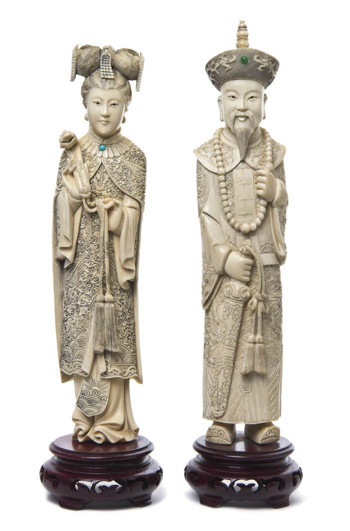 A Pair of Chinese Ivory Carvings of an Emperor and: A Pair of Chinese Ivory Carvings of an Emperor and Empress, both shown wearing embroidered robes, the man holding a sword and the woman a ruyi scepter, on hardwood stands. Height of taller ivory 11 in