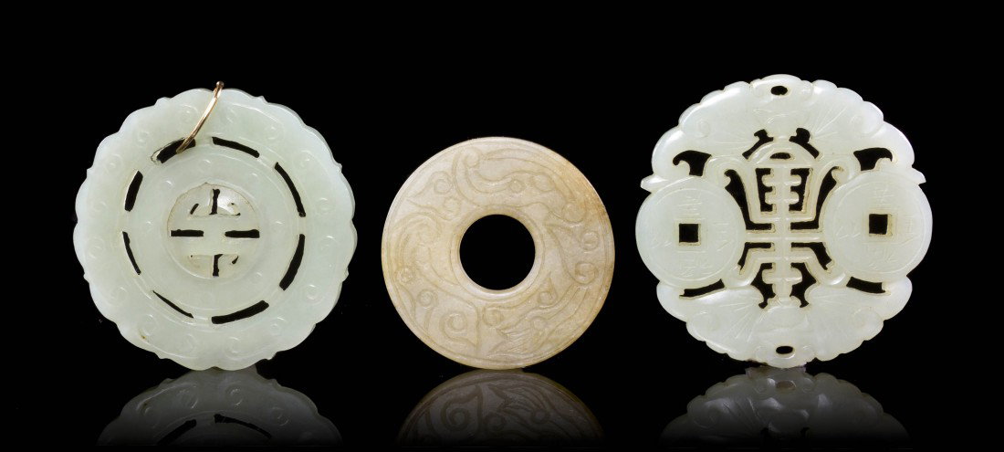 A Group of Three Jade Bi, Diameter of largest 2 1/: A Group of Three Jade Bi, one of celadon colored stone having a free-moving ring at the center, the second of two coins and two bats, and the third of tan colored stone with incised decoration. Diamet