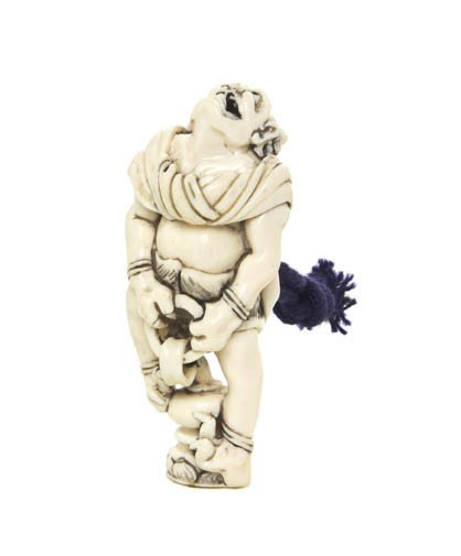 An Ivory Netsuke of an Oni, Height 2 5/8 inches.: An Ivory Netsuke of an Oni, the figure pulling on a chain mounted to a pedestal, facing upward and having inlaid eyes, having mark on the underside. Height 2 5/8 inches.