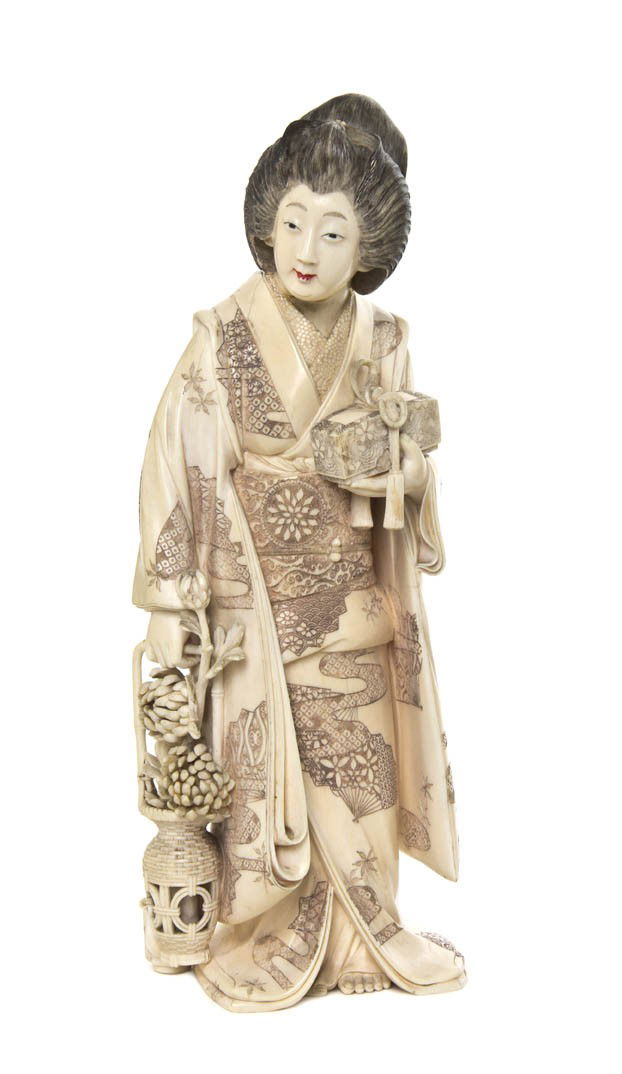 A Japanese Ivory Carving of a Woman, Height 10 1/2: A Japanese Ivory Carving of a Woman, depicting the robed figure with loosely coiffed hair, holding a lidded box in one hand and a basket of flowering chrysanthemums in the other, with a teapot by her