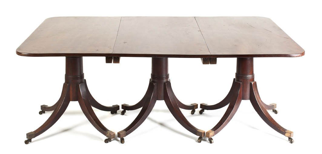 A Chippendale Style Mahogany Triple Pedestal Dining: A Chippendale Style Mahogany Triple Pedestal Dining Table, the rectangular top with rounded corners raised on quadripartite pedestal bases, ending in brass caps and casters, having servant buzzers on