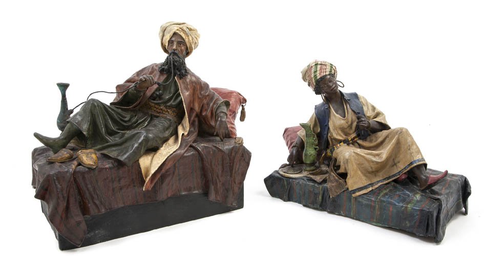 A Pair of Papier Mache Orientalist Figures, Width : A Pair of Papier Mache Orientalist Figures, each in reclining pose, the turbaned gentleman modeled smoking a hookah, the lady with ewer and platter. Width of wider 14 3/4 inches.