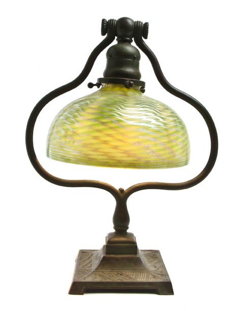 A Tiffany Studios Favrile Glass and Bronze Desk L: A Tiffany Studios Favrile Glass and Bronze Desk Lamp, having a circular damascene shade on a harp form base, base impressed Tiffany Studios New York, 665. Height 12 3/4 inches. Property from the Colle