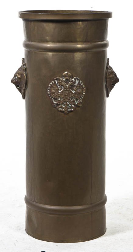 A Brass Umbrella Stand, Height 23 3/4 inches.: A Brass Umbrella Stand, of cylindrical form with applied lion mask handles and double headed English crest. Height 23 3/4 inches. Property from the Elne Elaine Russ Trust, Winnetka, Illinois