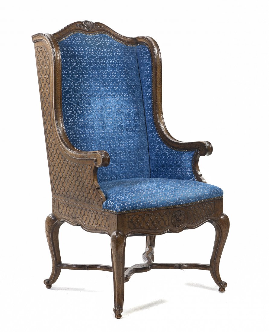 A French Provincial Style Wingback Armchair, Heig: A French Provincial Style Wingback Armchair, having a foliate carved crest rail over the upholstered back and seat, raised on cabriole legs joined by an X-form stretcher. Height 47 inches. Property fr