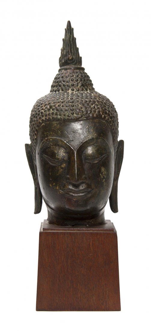 A Bronze Model of the Head of Buddha, Height of h: A Bronze Model of the Head of Buddha, the figure depicted forward facing with raised snail knots covering the head below the flame-form finial, raised upon a later black base. Height of head 11 1/2 in