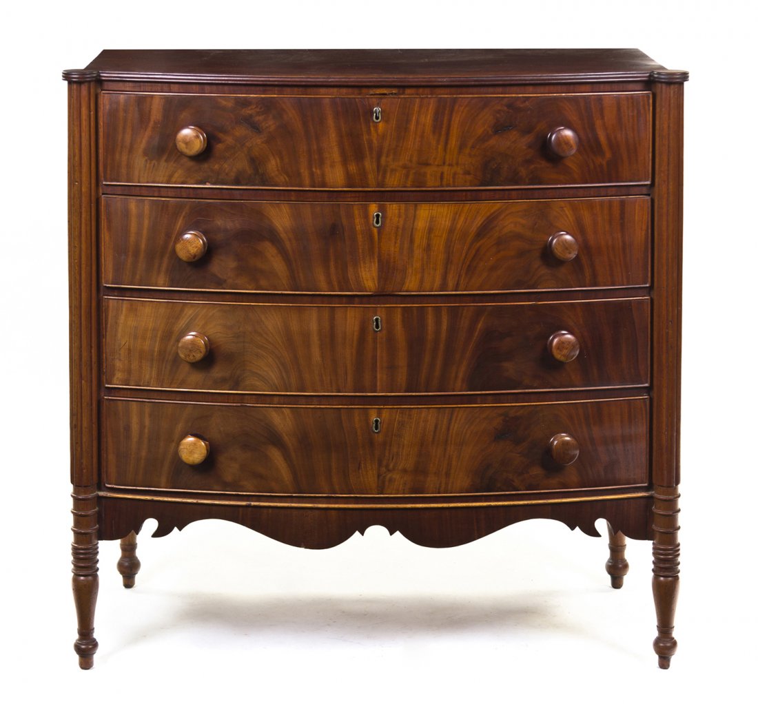 An American Sheraton Style Mahogany Chest of Drawe: An American Sheraton Style Mahogany Chest of Drawers, having a rectangular bowed top over four long drawers flanked by reeded columns above a shaped apron, raised on tapering legs ending in toupie fee