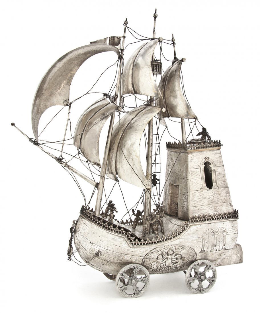 A German Silvered Metal Ship Form Trolley, Height: A German Silvered Metal Ship Form Trolley, of three mast form, set with sails and rigging, the ship's deck with various crew figures set on the body decorated with a cartouche centered by putti, the b