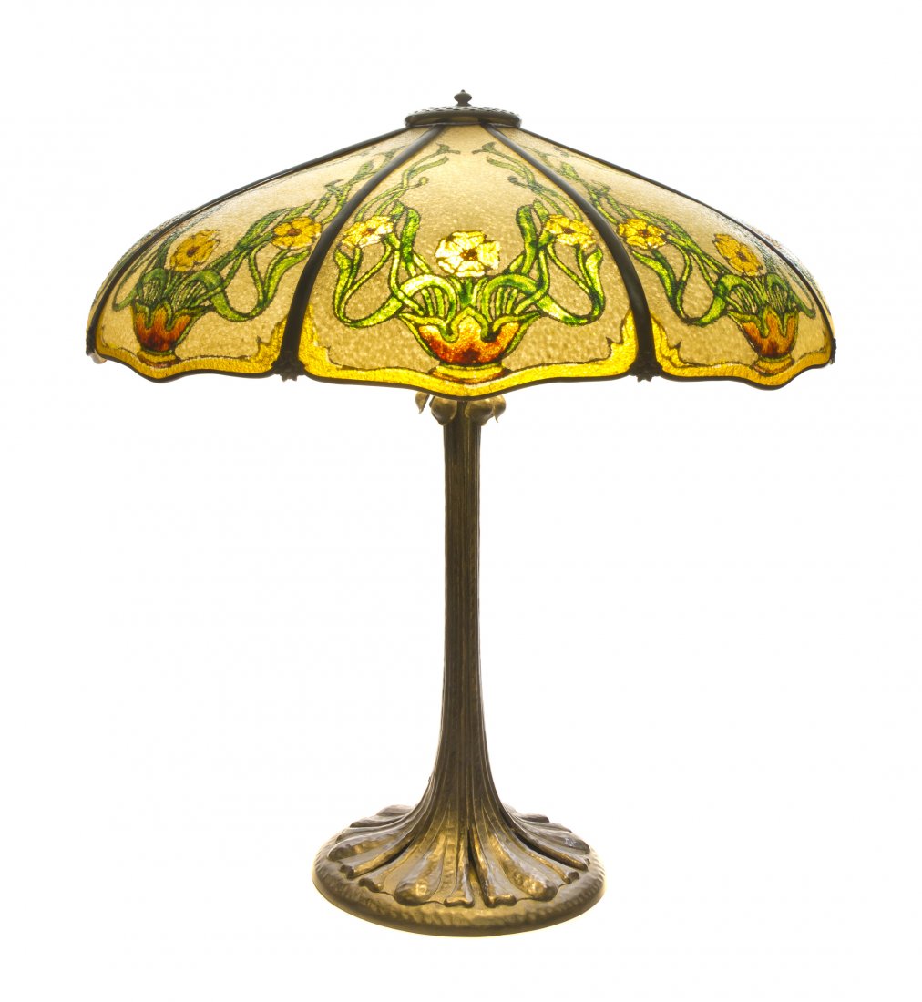 An American Arts and Crafts Panel Glass Lamp, Joh: An American Arts and Crafts Panel Glass Lamp, John Morgan and Sons, the domed shade having eight panels decorated with a jardiniere issuing flowers, raised on a hammered foliate form base. Diameter of