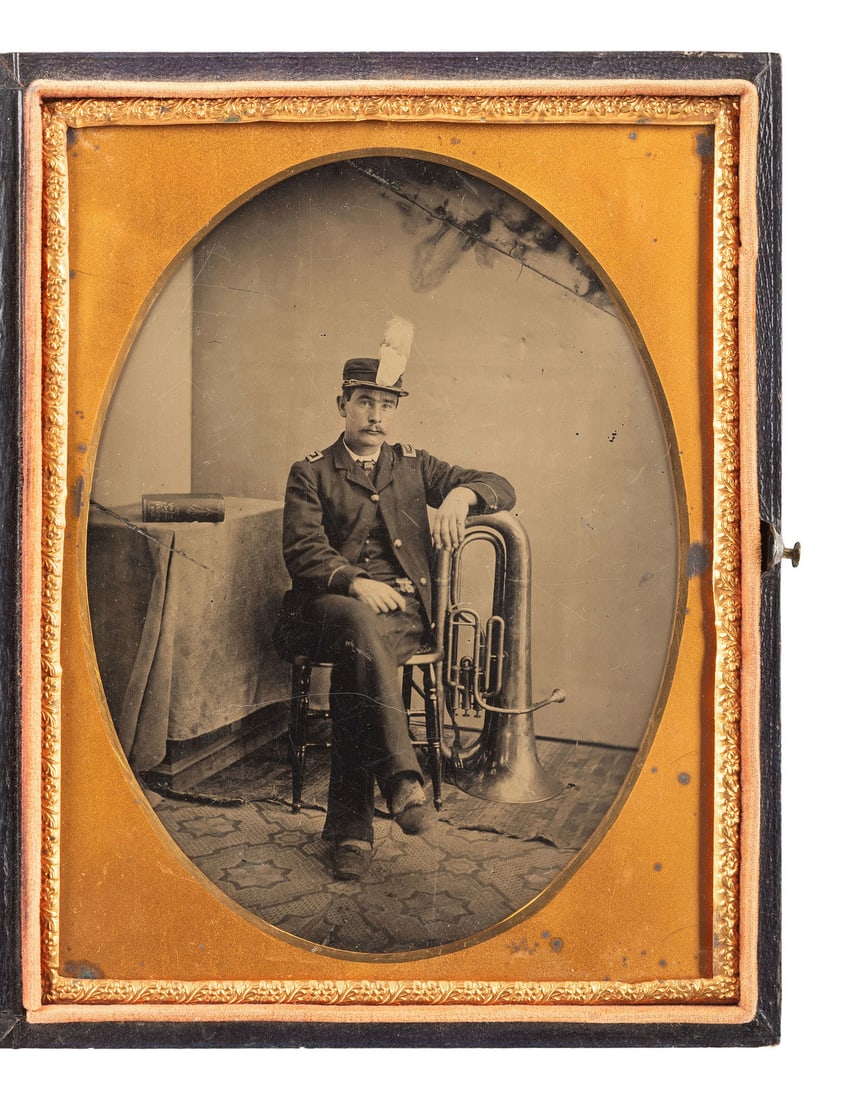 [EARLY PHOTOGRAPHY]. Half plate tintype of a band member with his sax horn. Ca 1890.: [EARLY PHOTOGRAPHY]. Half plate tintype of a band member with his sax horn. Ca 1890. Half plate tintype portrait of a band member in uniform, complete with plumed hat, seated in a studio and resting h