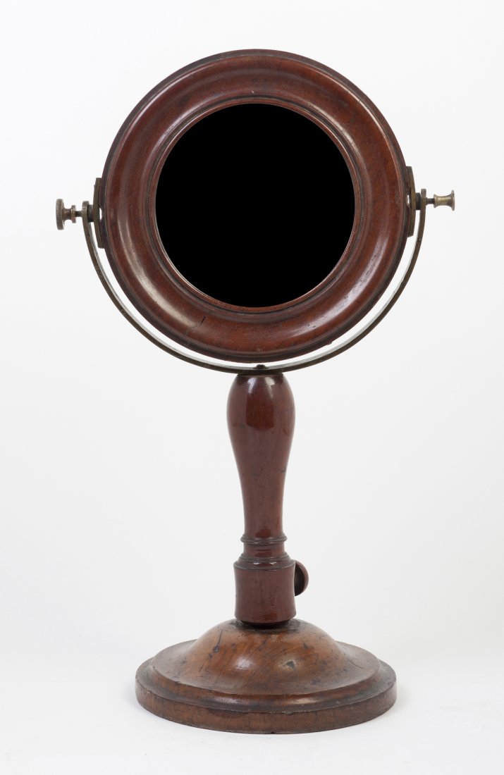 An American Mahogany Shaving Mirror, Height 20 in: An American Mahogany Shaving Mirror, the circular plate set in a conforming molded frame, raised a on circular foot. Height 20 inches. Property from the Estate of Helen and C. Nicholas Johnson, Jr., C