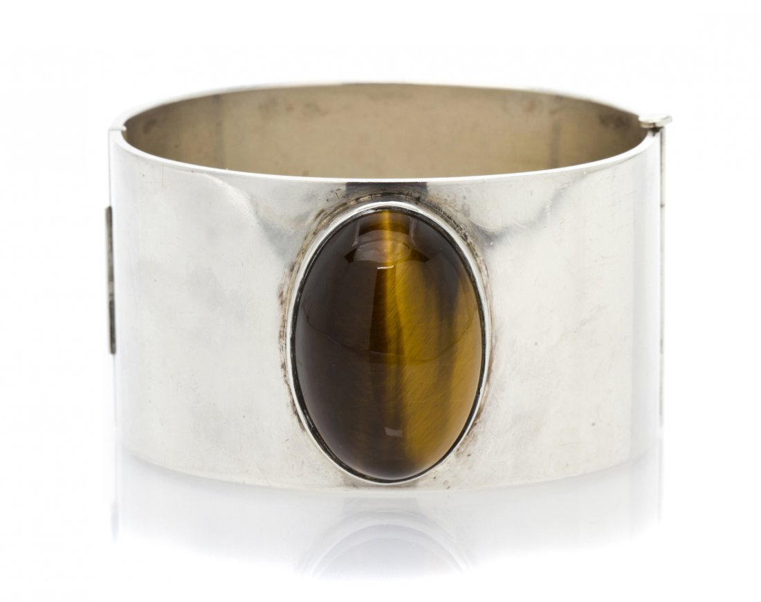 A Sterling Silver and Tiger's Eye Cuff Bracelet, K: A Sterling Silver and Tiger's Eye Cuff Bracelet, Kaunis Koru, Finland, containing one oval cabochon cut tiger's eye measuring approximately 30.00 x 20.00 mm within a hinged cuff setting. Stamp: (Maker