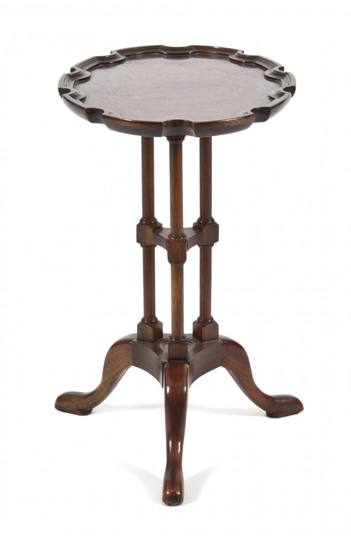 An American Mahogany Candle Stand, Baker, Height 2: An American Mahogany Candle Stand, Baker, Historic Charleston Reproduction, having an oval burlwood top with a scalloped edge, set on three columnar supports joined by a medial shelf, raised on tripod