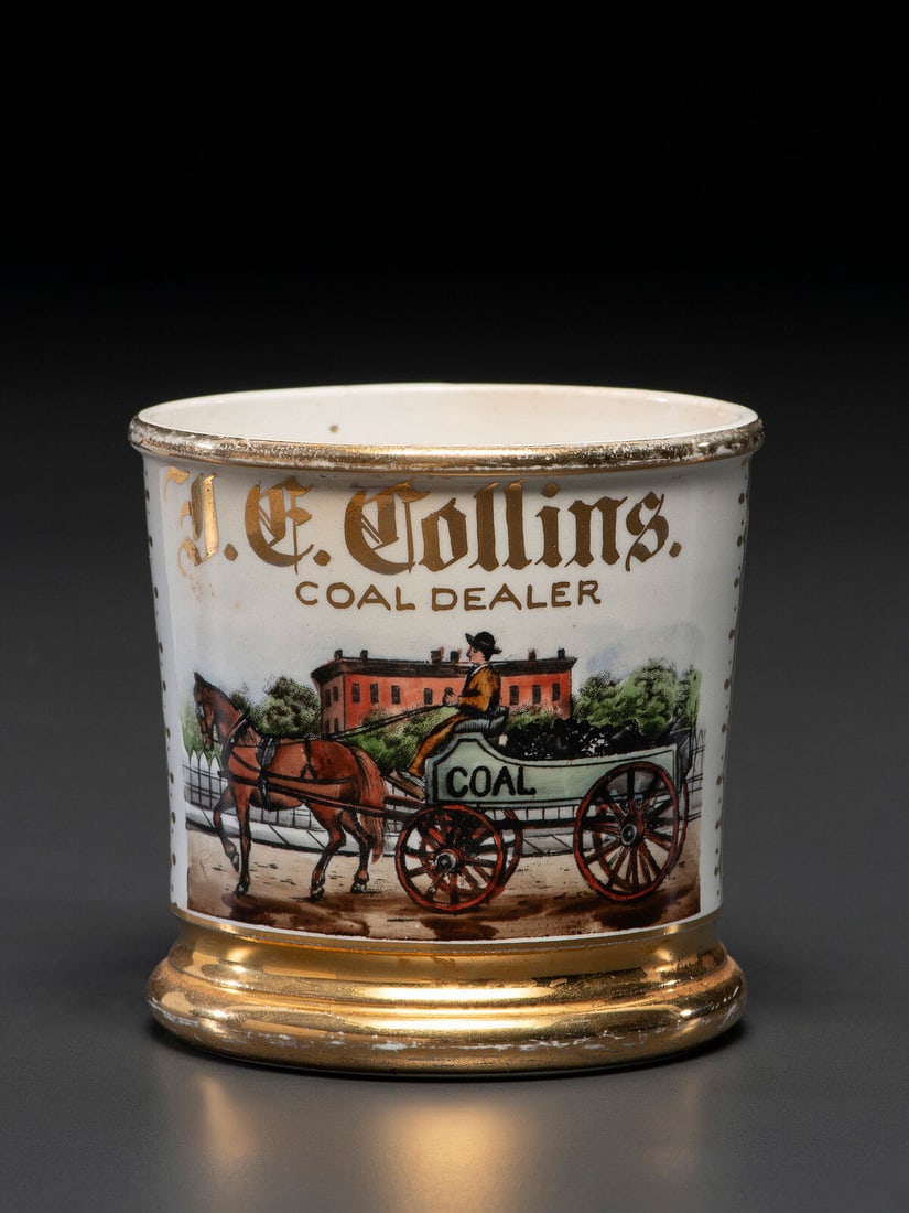 A Coal Dealer's Porcelain Occupational Shaving Mug: A Coal Dealer's Porcelain Occupational Shaving Mug Late 19th/Early 20th Century bearing the name J.C. Collins and Coal Dealer in gilt lettering, depicting a gentleman driving a horse drawn coal wagon.