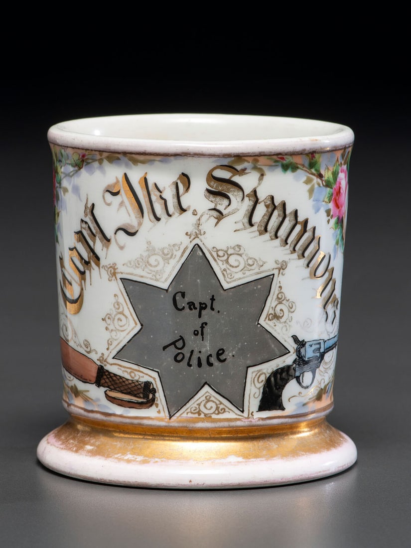 A Police Captain's Porcelain Occupational Shaving Mug: A Police Captain's Porcelain Occupational Shaving Mug Early 20th Century with the name Capt. Ike Simmons in gilt lettering against a peach wrap and a floral motif, with a police badge that reads Capt.