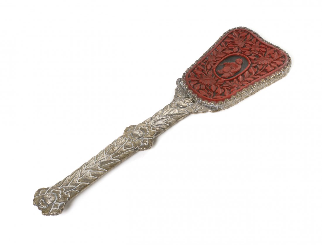A Chinese Two-Color Cinnabar Lacquer and Silver Ha: A Chinese Two-Color Cinnabar Lacquer and Silver Handled Mirror, the shaped mirror having cinnabar lacquer over black lacquer depicting a figure at the center surrounded by blossoming flowers, the hand