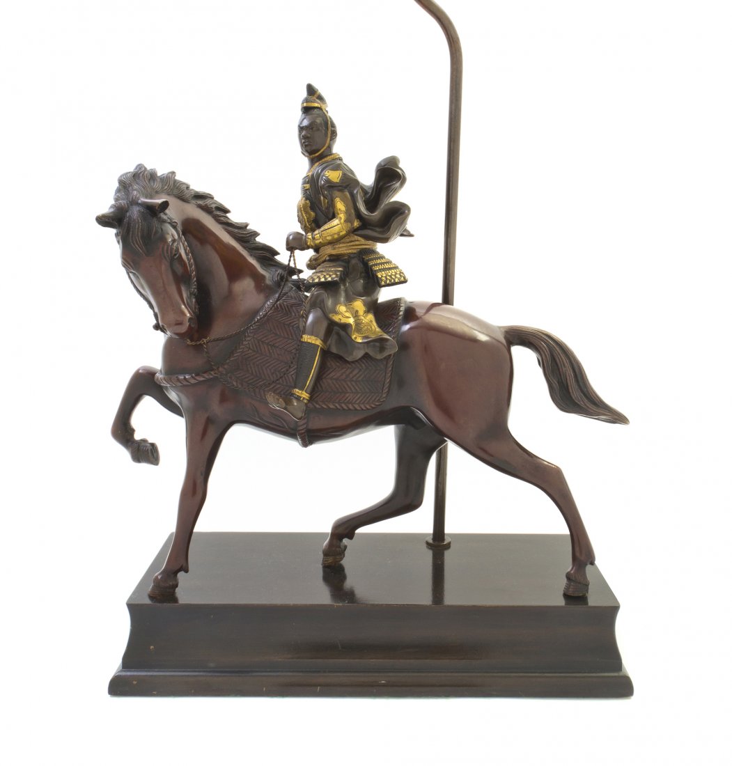 A Japanese Mixed Metal Model of a Samurai Warrior: A Japanese Mixed Metal Model of a Samurai Warrior on Horseback, Meiji Period, depicting a samurai warrior clutching the reins, wearing armor with gilt highlights, the horse in motion, their heads turn