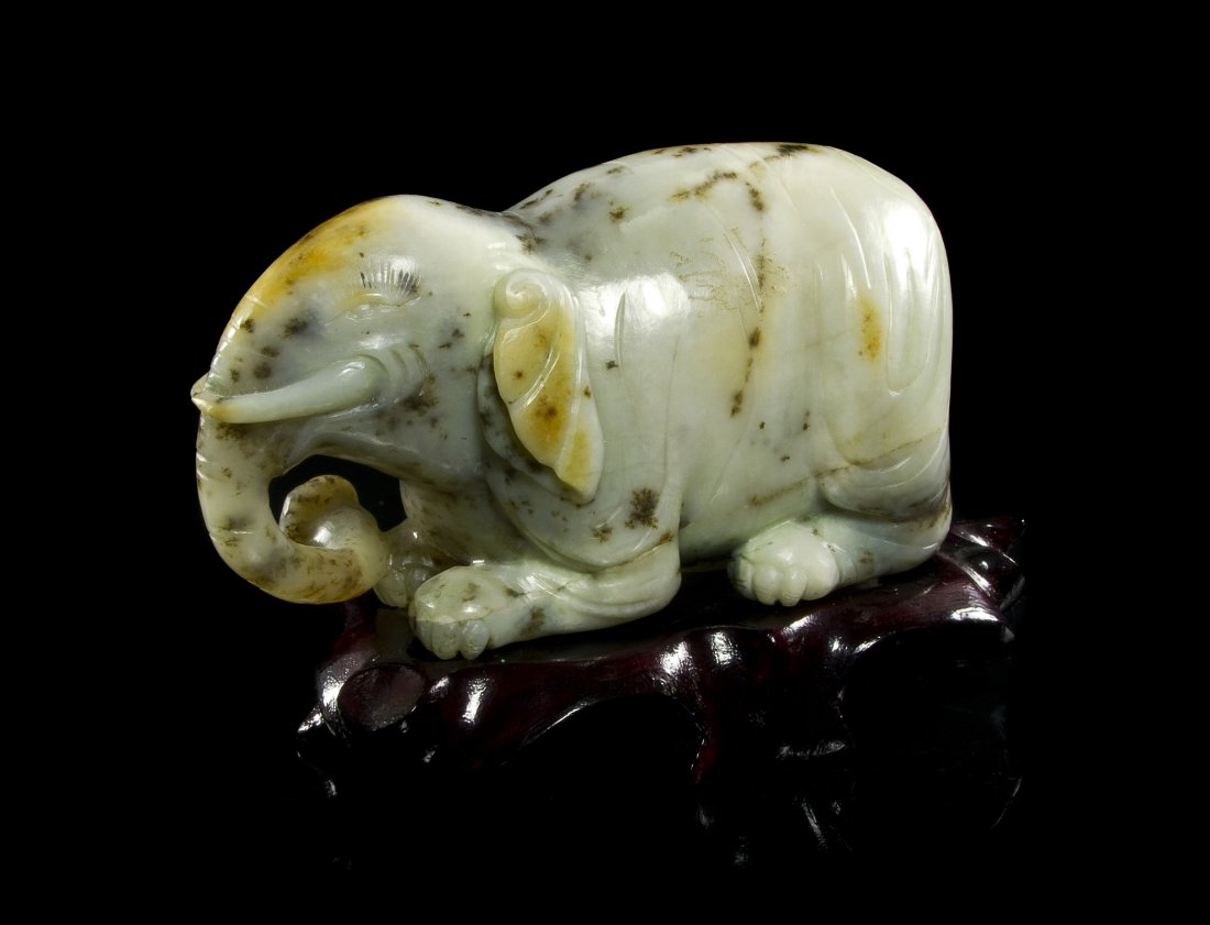 A Hardstone Carving of an Elephant, Length 5 1/2 i: A Hardstone Carving of an Elephant, of white stone with black speckles, depicting the animal in a recumbent pose with head raised, set atop a fitted hardwood base. Length 5 1/2 inches. Property of a P