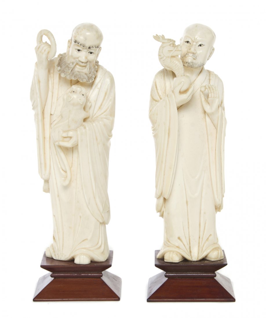 A Pair of Chinese Carved Ivory Figures of Immortal: A Pair of Chinese Carved Ivory Figures of Immortals, one depicted carrying a fu dog pup in one hand and a ring in the other, the other figure holding a large pearl issuing a dragon head, each raised o
