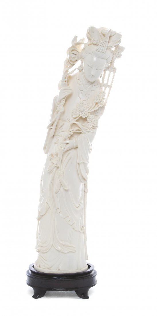A Carved Ivory Tusk of a Lady, Height 13 inches.: A Carved Ivory Tusk of a Lady, depicted with carved decoration to her embroidered robe and with elaborate headdress and a ruyi necklace, in a standing pose holding flowering branches, raised on a wood