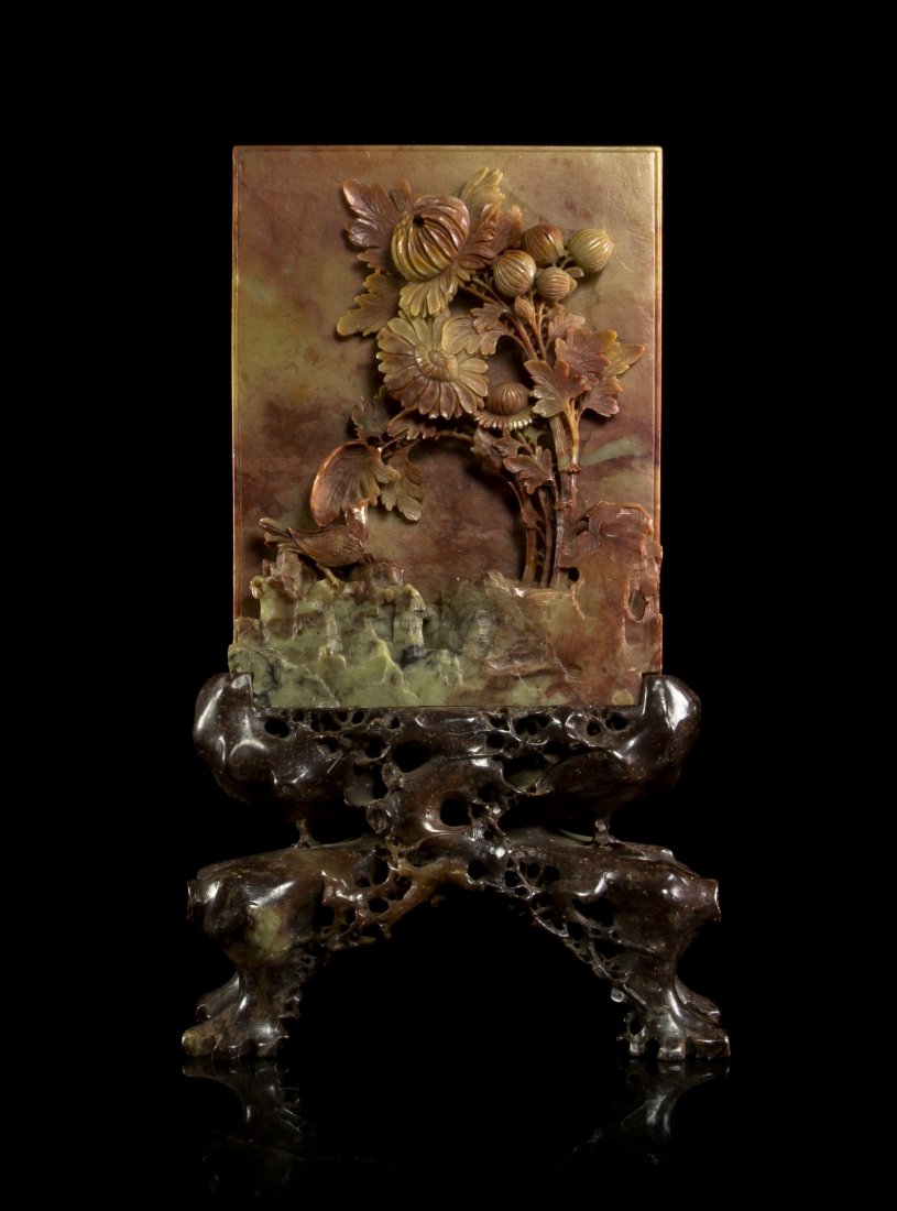 A Chinese Carved Steatite Table Screen, Height ove: A Chinese Carved Steatite Table Screen, of olive green and red colored stone, of rectangular form and having carving in relief of a flowering plant, raised in a carved stone base resembling a burled r
