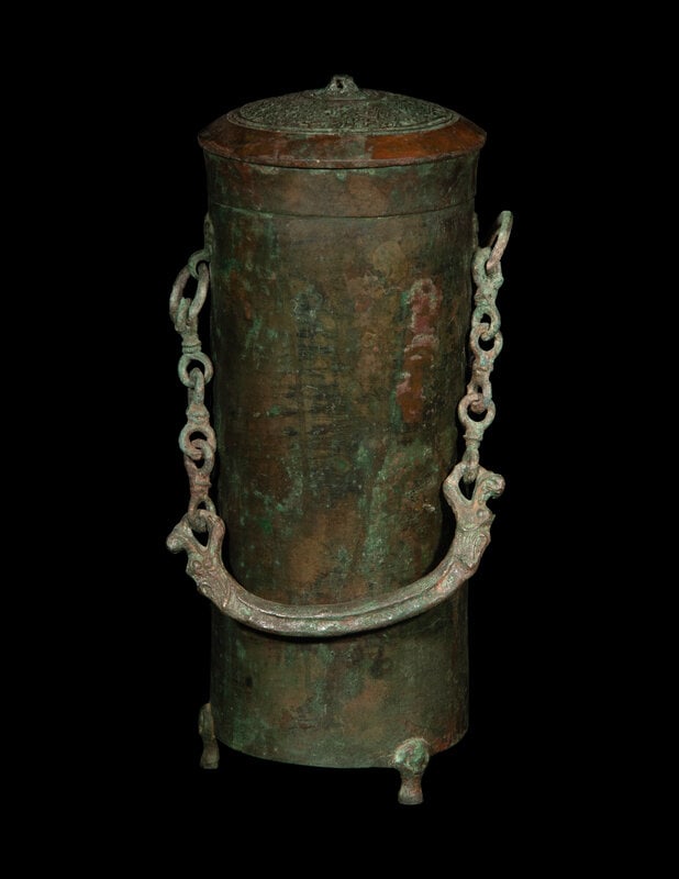 A Chinese Bronze Handled Wine Vessel, Xing: A Chinese Bronze Handled Wine Vessel, Xing Possibly Eastern Zhou Period, Circa 470-370 B.C. with the cylindrical body flanked by loose chain-link jhandles, supported on threee short cabriole legs