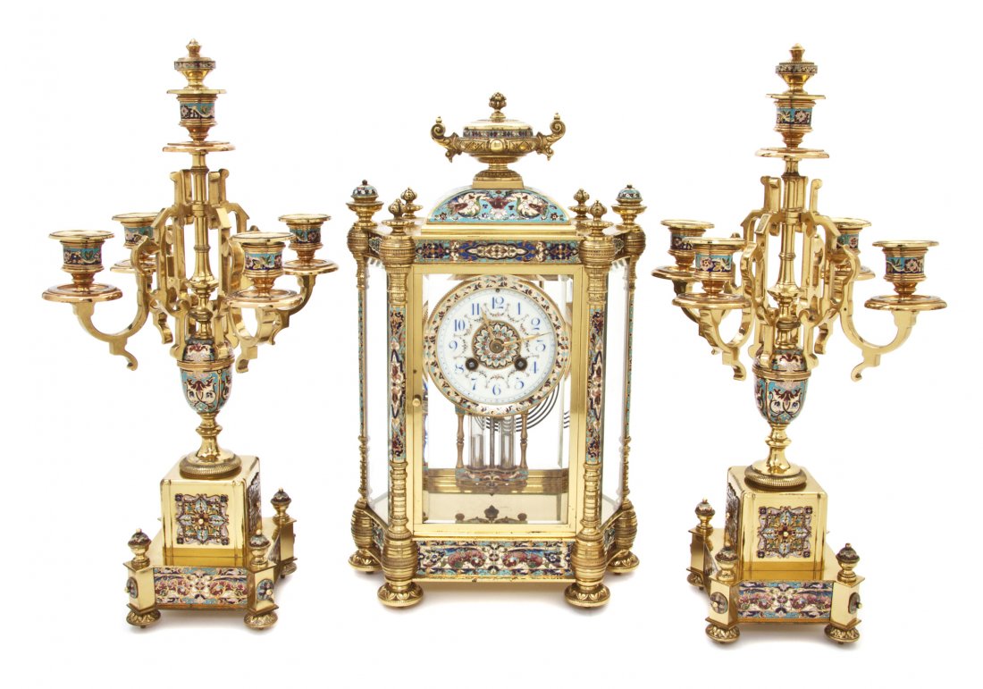 A French Gilt Brass and Champleve Clock Garniture,: A French Gilt Brass and Champleve Clock Garniture, the clock having an elongated hexagonal case with an urn finial over a circular dial with Arabic numerals and painted floral swags, with Adolphe Moug