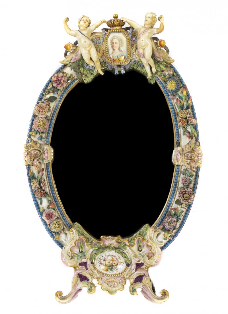 A Meissen Porcelain Mirror, Height 33 x width 19 1: A Meissen Porcelain Mirror, having a shaped oval beveled plate beneath the putti and crown portrait crest, having applied floral and bird decoration throughout, with crossed swords in underglaze blue.