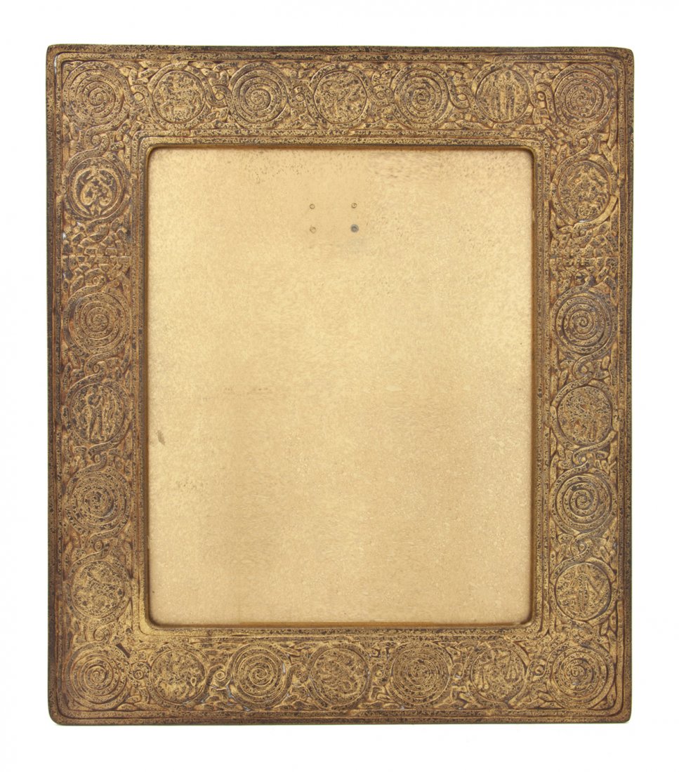 A Tiffany Studios Gilt Bronze Frame, Height 14 1/: A Tiffany Studios Gilt Bronze Frame, in the Zodiac pattern, the rectangular frame having a dore finish, the backplate stamped Tiffany Studios, New York, 925. Height 14 1/8 x width 12 1/8 inches. Prope