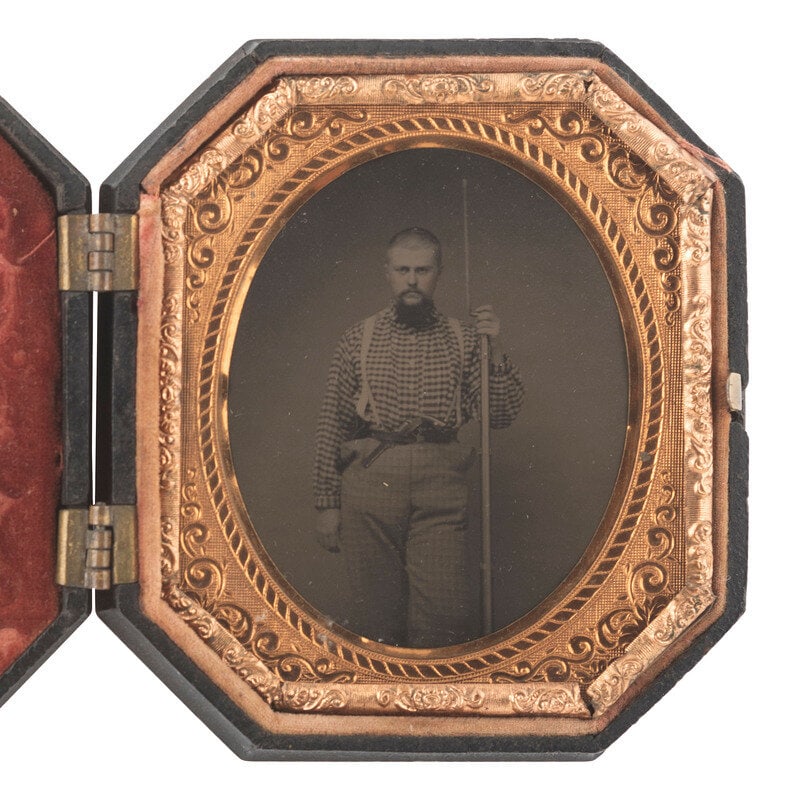 [CIVIL WAR]. Sixth plate tintype of a doubly armed soldier with shaved head, possibly Confederate.: [CIVIL WAR]. Sixth plate tintype of a doubly armed soldier with shaved head, possibly Confederate. Standing portrait of a bearded tough wearing essentially civilian clothing including a gingham shirt,
