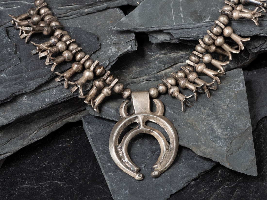 Navajo Child's Squash Blossom Necklace, Collected by Hoffman Birney (1891-1958): Navajo Child's Squash Blossom Necklace, Collected by Hoffman Birney (1891-1958) ca 1900 twenty-two petite squash blossoms with chiseled accents; sandcast double-crescent naja with horned design neckla