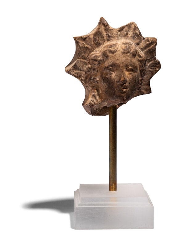 A Greek Terracotta Head of Helios: A Greek Terracotta Head of Helios Circa 3rd-2nd Century B.C. Height 2 3/8 inches (6.03 cm). Size Height 2 3/8 inches (6.03 cm). Condition Height with stand 4 3/4 inches (12.