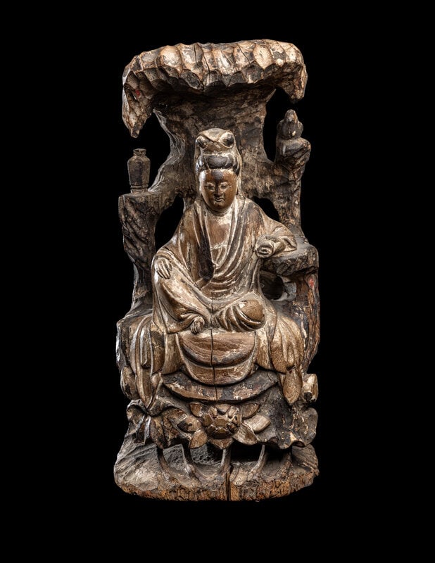 A Chinese Carved Wood Figure of Guanyin: A Chinese Carved Wood Figure of Guanyin Qing Dynasty (1644-1912) the deity depicted seated at ease on a raised pedestal backed by a tree, flanked by a vase and a bird, her left hand bearing a scroll a