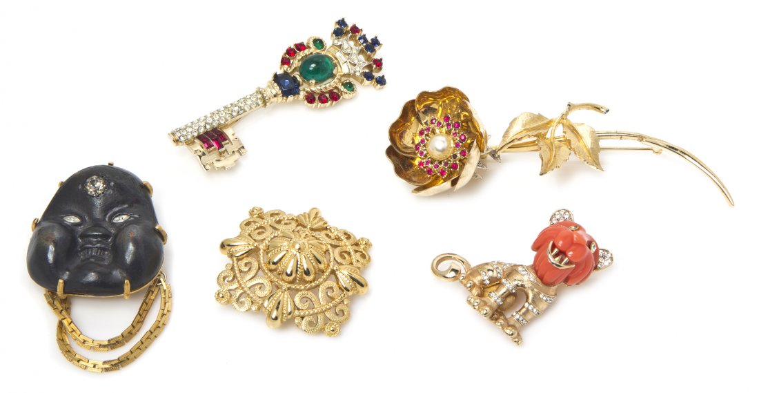 A Group of Five Brooches,: A Group of Five Brooches, comprised of a multigem and rhinestone key stamped Trifari, a Buddha face stamped Trifari, a faux carved coral lion stamped Boucher, an articulated flower stamped Boucher, an