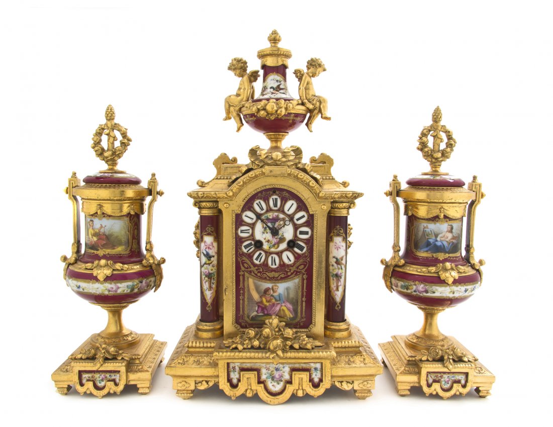 A Sevres Style Porcelain and Gilt Metal Mounted C: A Sevres Style Porcelain and Gilt Metal Mounted Clock Garniture, the clock having an urn form finial flanked by winged putti, above the arched case set with a circular dial with Roman hours over a cou