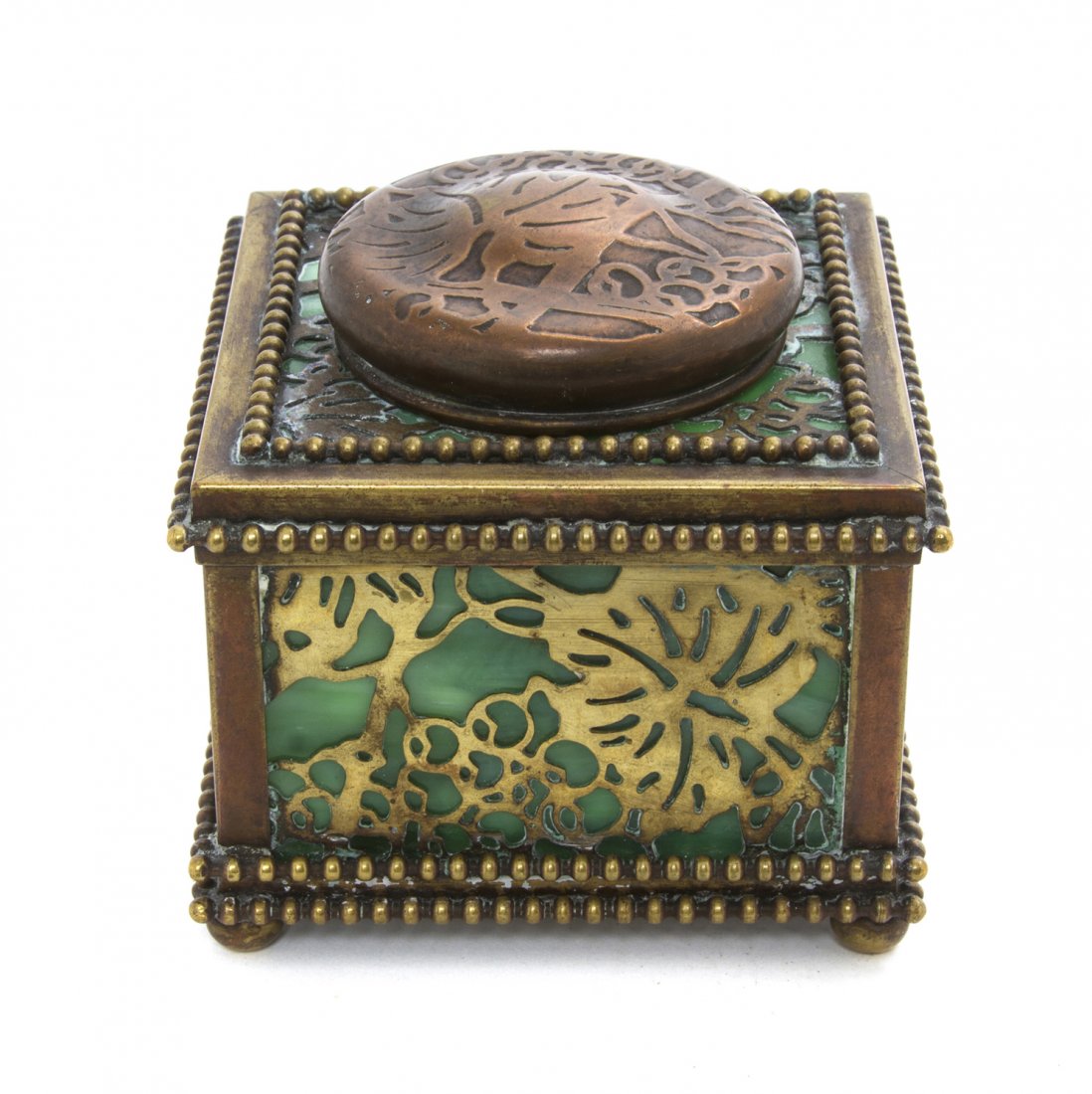 A Tiffany Studios Gilt Bronze and Favrile Glass I: A Tiffany Studios Gilt Bronze and Favrile Glass Inkwell, in the Grapevine pattern, the circular lid opening to a glass well over the square body set with green slag glass, raised on squat feet. Width 