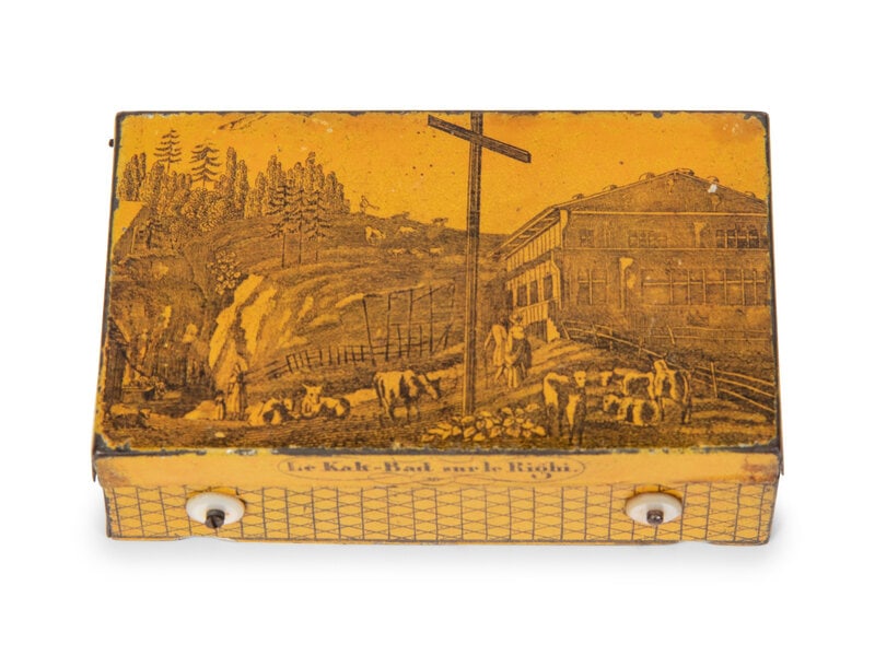 A Musical Movement in a Tin Transfer Box : A Musical Movement in a Tin Transfer Box with 2 1/2 inch cylinder, sectional comb, and teeth in groups up to five, the lid depicting Le Kak-Bad sur le Righi. Height 1 1/2 x width 3 1/2 x