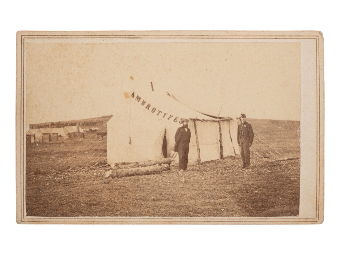[CIVIL WAR]. CDV of a photographer's tent reading "AMBROTYPES," with the likely photographer and an: [CIVIL WAR]. CDV of a photographer's tent reading "AMBROTYPES," with the likely photographer and an officer standing just outside. Alexandria, VA: Gorman & Jordan, ca 1864. CDV on cardstock mount with
