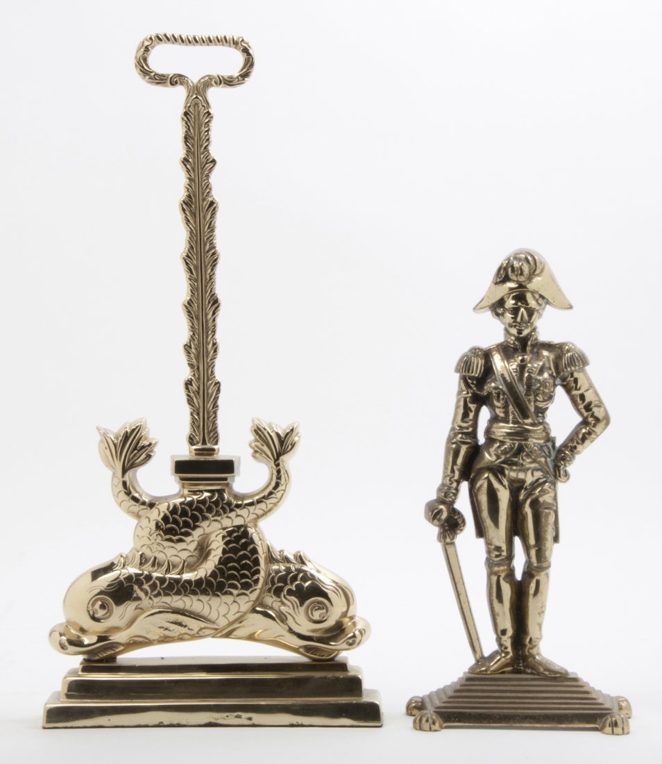 A Victorian Brass Doorstop, Height of first 13 1/4 inch: A Victorian Brass Doorstop, in the form of a standing general, together with a later example having entwined dolphins. Height of first 13 1/4 inches.