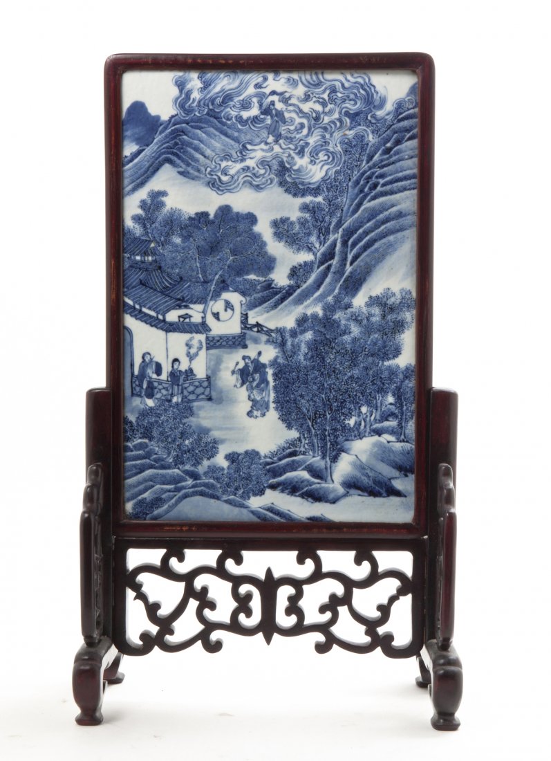 A Chinese Porcelain Table Screen, Height of porcelain 1: A Chinese Porcelain Table Screen, having blue and white decoration depicting a deity emerging from scrolling clouds above figures in a garden, mounted in a carved wood stand. Height of porcelain 15 x 