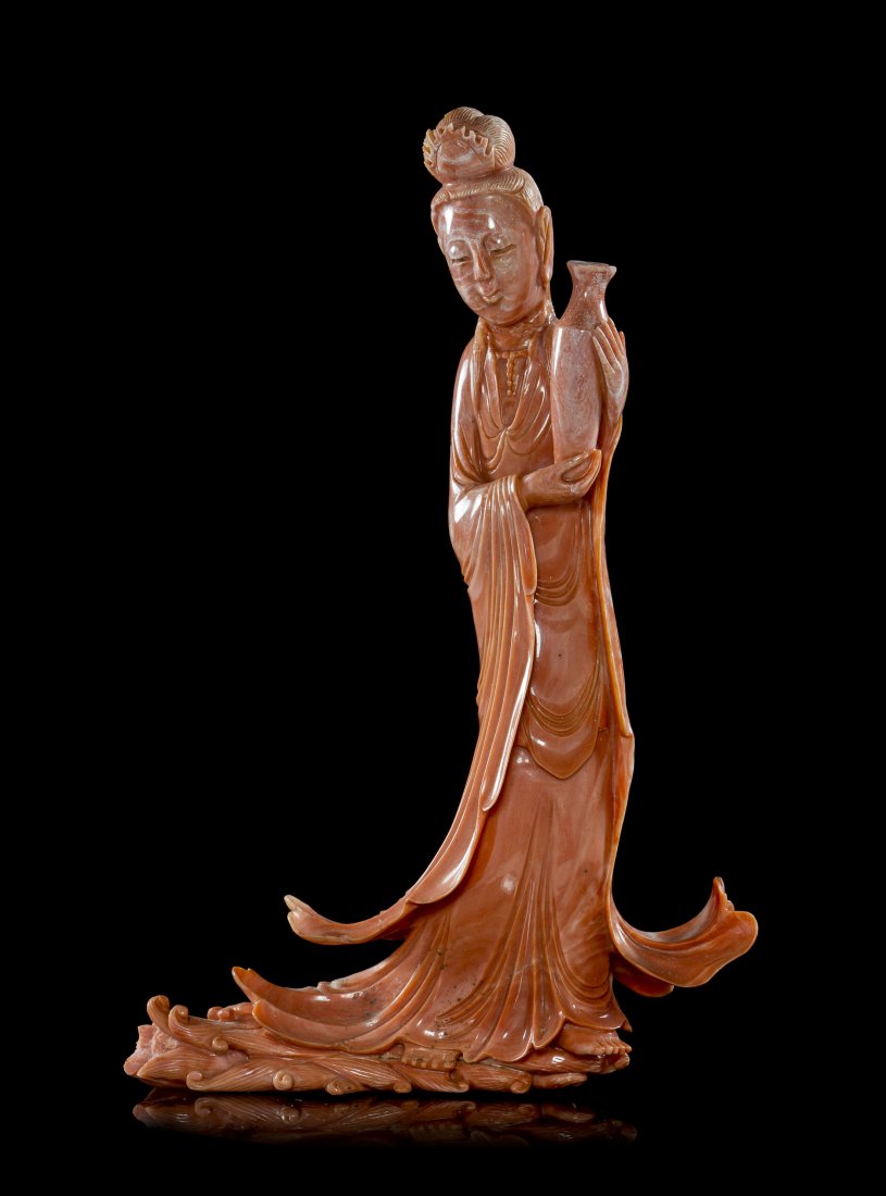 A Chinese Carved Coral Figure of Guanyin, Height 6 7/8 : A Chinese Carved Coral Figure of Guanyin, depicted holding a baluster-form bottle, in draped robes cascading down to scrolling waves. Height 6 7/8 inches.