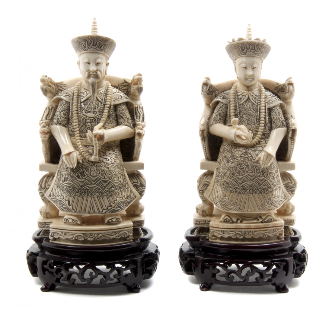 A Pair of Chinese Carved Ivory Figures of an Emperor an: A Pair of Chinese Carved Ivory Figures of an Emperor and Empress, each depicted with elaborate crown and robes in a carved throne, the man holding his court necklace and the lady with a ruyi scepter, 