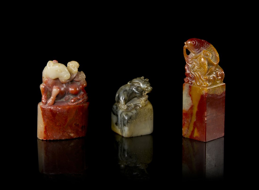 A Group of Three Chinese Stone Carved Seal Stamps, Heig: A Group of Three Chinese Stone Carved Seal Stamps, the first of a red to caramel soapstone, surmounted by two fishes on swirling waves, another of a red and near-white stone, surmounted by a monkey ri