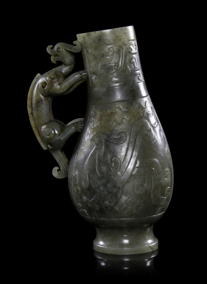 A Carved Jade Jug-Form Vessel, Height 8 1/8 inches.: A Carved Jade Jug-Form Vessel, of a mottled green stone with russet inclusions and veining, having a qilong-form pierce carved handle and archaistic relief carved decoration throughout, raised on a ci
