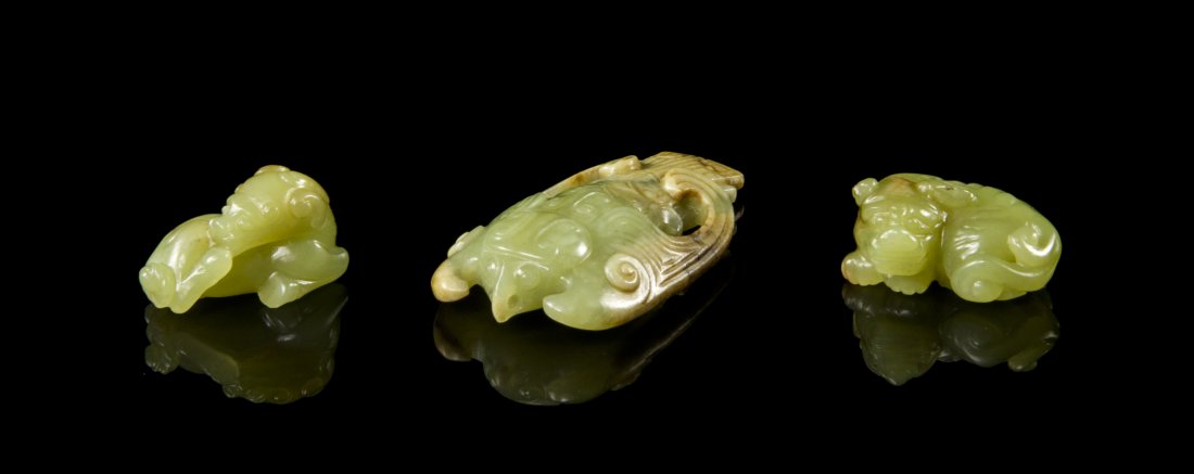 A Group of Three Yellow Jade Toggles, Width of widest 2: A Group of Three Yellow Jade Toggles, the first depicting an archaistic bird, the second and third modeled after recumbent lions. Width of widest 2 3/8 inches.