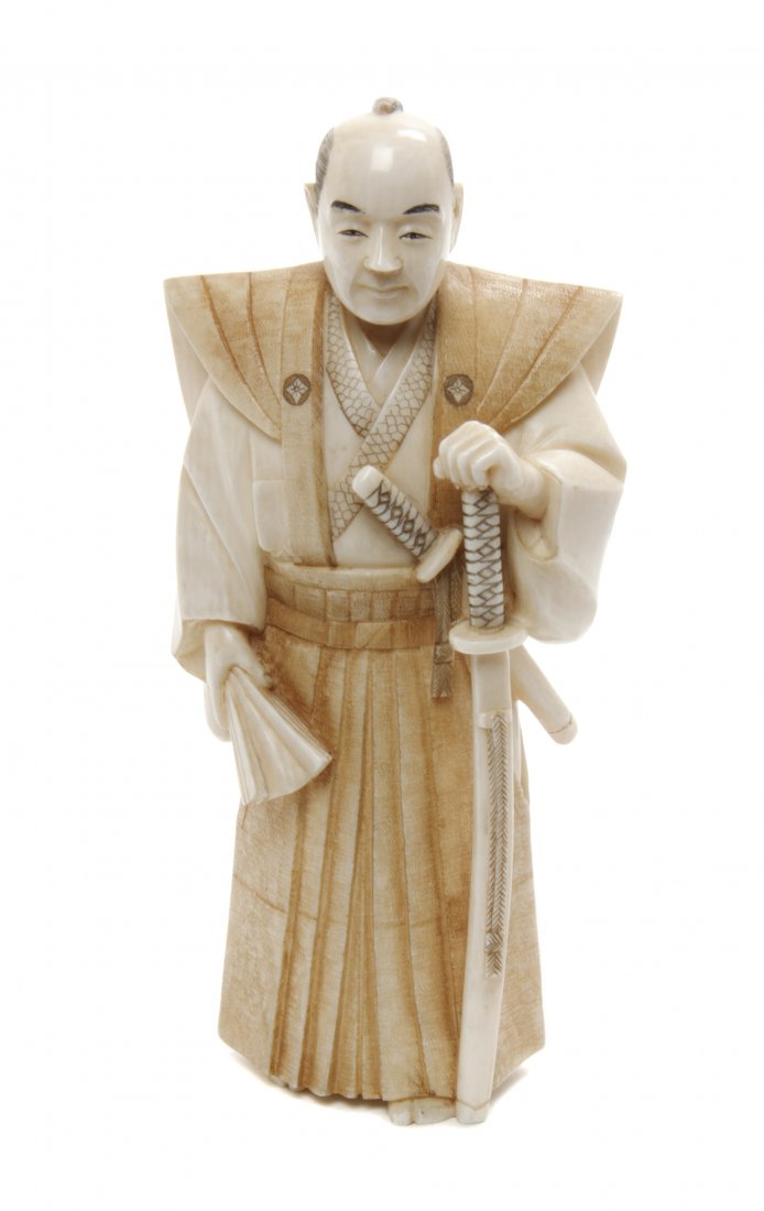 A Japanese Carved Ivory Okimono, Height 5 1/4 inches.: A Japanese Carved Ivory Okimono, depicting a standing samurai, the figure depicted with his katana in one hand and a folding fan in the other, signed to the underside. Height 5 1/4 inches. Property fr
