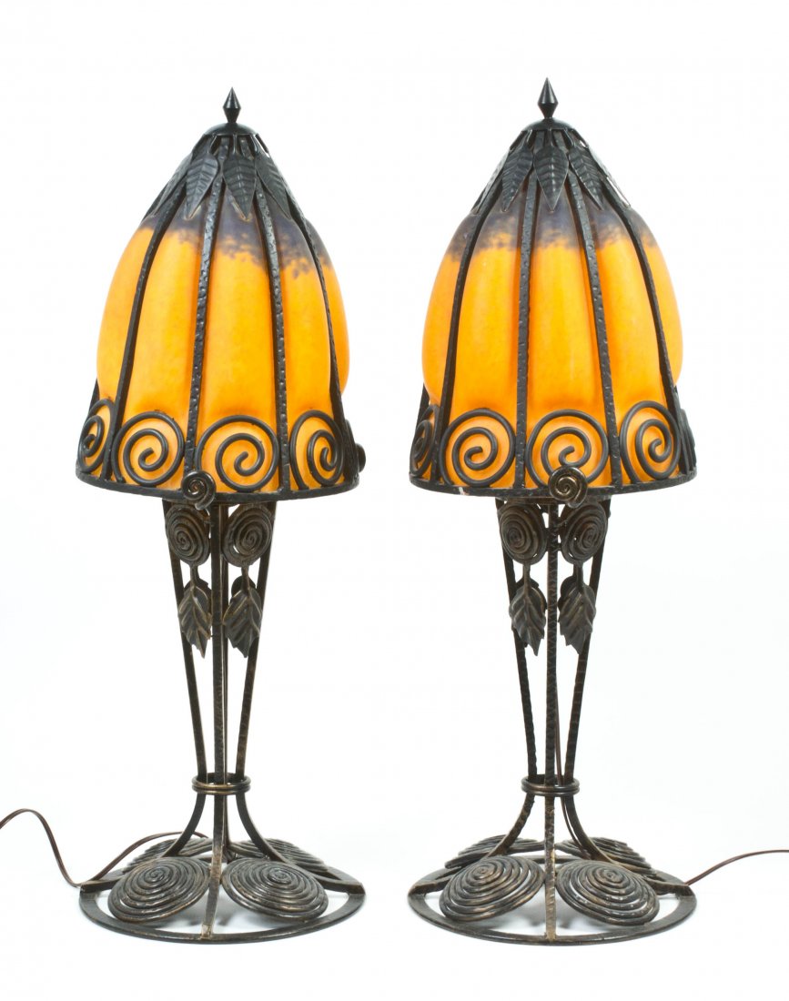 A Pair of Art Deco Style Iron and Glass Table Lamps, in: A Pair of Art Deco Style Iron and Glass Table Lamps, in the manner of Charles Schneider, the blown glass bell form shades within linear wrought iron ribs, further having leaf and scrolled decoration, 