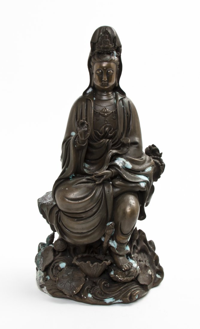 A Bronze Figure of Guanyin, Height 12 5/8 inches.: A Bronze Figure of Guanyin, depicted in flowing robes, seated upon a naturalistic base with lotus and scrolling waves. Height 12 5/8 inches.